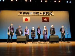 イザベラ・ア・カペラの方々が「大和高田市成人祝賀式」と書かれたステージ上で1列に並び歌を歌っている写真