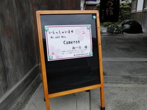 木のフレームの案内板に「いらっしゃいませ Mr. and Mrs. Cameron 御一行様」と書かれた紙が貼られてある写真