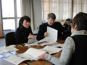 手前に女性1人、奥に女性とキャメロンさんが座り、机に広げられた資料を見ながら話し合いが行われている写真