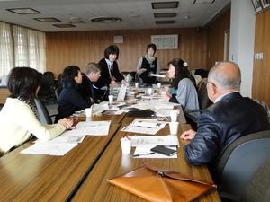 長机を向かい合わせに付けて並べた席の左側に女性2人とキャメロンさん、右側に女性1人と男性1りが座り、机の奥に女性2人が立って話し合いが行われている写真