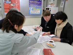 手前に座っているグレーのジャケットを着た女性が、キャメロンさんと女性が見ている資料を指しながら話をしている様子の写真