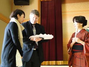 着物を着た女性の横で、黒のスーツを着たキャメロンさんが開いた扇子を手に持ち見ている写真