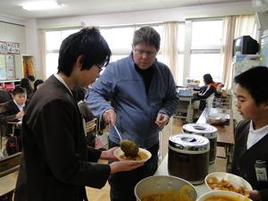男子生徒が持っている器にカレーを注いでいるキャメロンさんの写真