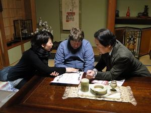 女性と、キャメロンさんと、スーツを着た男性が座卓に座り、座卓に広げられた資料を見ている写真