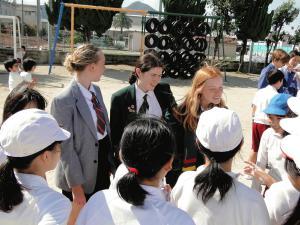 リズモー市からの女子学生3名が運動場で陵西小学校の子供たちに囲まれている写真