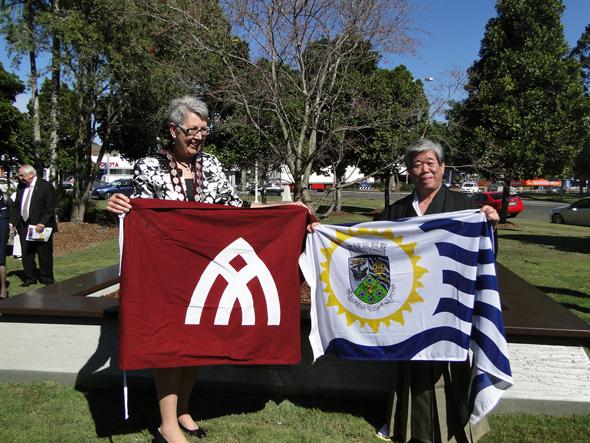 両市長がそれぞれの市旗を持ち並んで記念撮影をしている写真