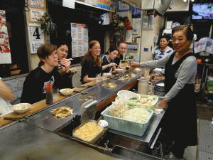 広島焼を鉄板のあるカウンターで食べているリズモー市からの学生5名の写真