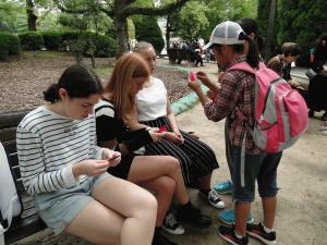 小学生がベンチに座るリズモー市の女子学生3人に鶴の折り方を教えている写真