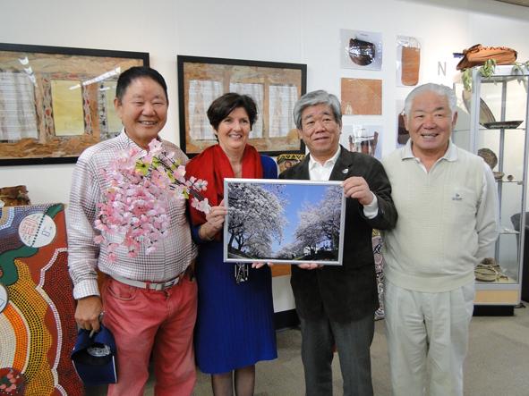 市長とオーストラリア人の女性が桜の写真を一緒に持ち、両側に日本人男性が立って記念撮影をしている写真