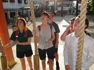 龍王宮の賽銭箱前で鳴らしている鈴を見上げているリズモー市の学生達の写真