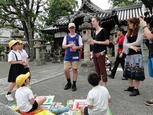明日香村の神社の前で絵を描いている子供達と話をしているリズモー市の学生たちの写真