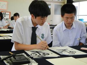 高田商業高等学校の男子生徒とリズモー市の男子学生が隣同士で書道をしている写真