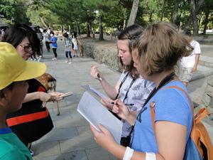 屋外でリズモー市の学生が手にノートとペンを持ちメモを取っている様子の写真