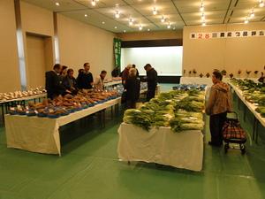 第28回農産物品評会でいろいろな種類の野菜が机の上に展示されているのを見ているたくさんの人達の写真
