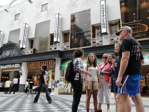 なんばグランド花月の大きな建物の前に集まっているリズモー市の男性と女性、女子学生3人の写真