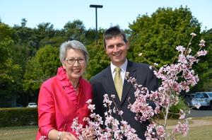 ピンクの花を咲かせている枝を前にして、ピンク色の服を着た市長Jenny Dowellさんとスーツを着たゼネラルマネージャーのGary Murphyさんが笑顔で写っている写真