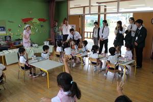 リズモー市の学生達が入り口に横一列で並び、一人の学生が園児とハイタッチしている磐園幼稚園児の給食の時間の写真