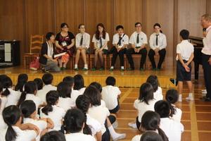 体育館の前に準備された椅子に一列で座っているリズモー市の学生達に磐園小学校の生徒一人が話をしている写真
