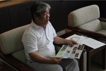 男性が写真が載った資料を広げながら椅子に座る前方を見ている写真
