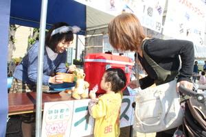 小さな子供とお母さんが購入した品物を、女子学生が手渡ししようとしている写真