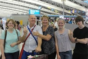 リズモー市の学生3人と関係者の男性と女性が空港で記念撮影をしている写真