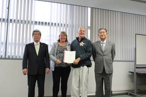 コリーンさんリックさん夫妻が委任状を2人で持ち両隣に村島会長・吉田市長が並んでいる写真