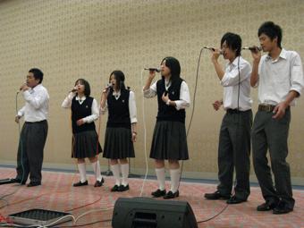 制服を着た男子学生3名と、女子学生3名がマイクを持って歌を歌っている写真