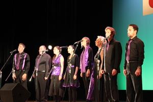 黒と紫色の衣装を着たイザベラ・ア・カペラの方々が、マイクの前で歌っている写真