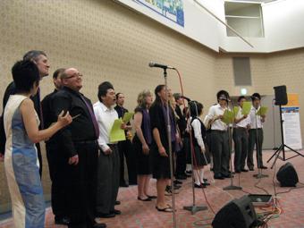 イザベラ・ア・カペラの方と緑色の紙を持った日本人学生達が一緒に歌を歌っている写真