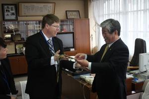 キャメロンさんが吉田市長に何かを手渡し、笑顔で受け取っている吉田市長の写真