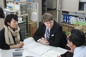 女性とキャメロンさんと男性が1つのテーブルに座り、キャメロンさんが男性の職員の方を見て話を聞いている写真