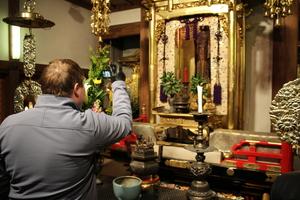 金色に装飾された仏壇をカメラで撮影しているキャメロンさんの後ろ姿の写真