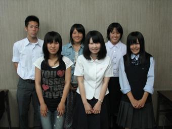 制服や私服を着た女子学生5名と、制服を着た男子学生1人が前後に3人ずつ並んで集合写真を撮っている写真