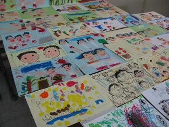 色々な色画用紙に顔などが描かれた沢山の絵が机に並べられている写真