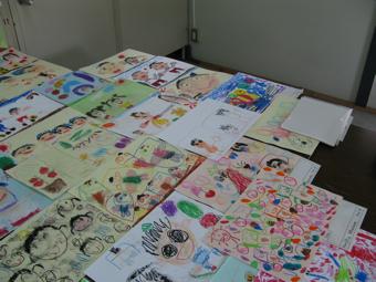 クレヨンで描かれている顔などの絵が机に並べられている写真