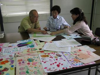 女性2人と男性1人が机に置かれた紙を指差しながら話し合いをしている様子の写真