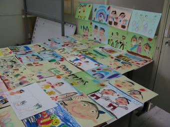 壁に貼られた8枚の絵と、机いっぱいに並べられた絵の写真