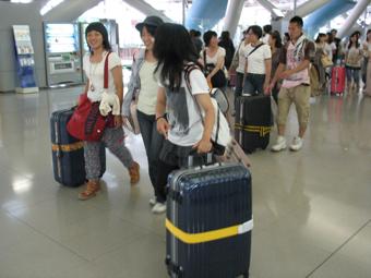 大きなキャリーケースを持って空港ロビーを笑顔で歩いている学生たちの写真