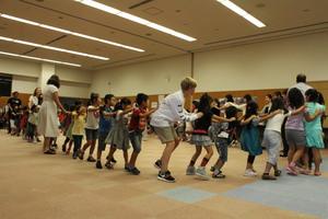 派遣学生、子供達で前の人の肩に両手を置き繋がって歩いている写真