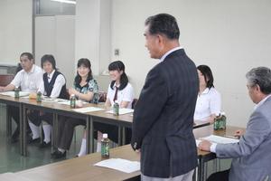派遣学生や関係者が並べられた長机に座り、男性が手前に立ち説明会が行われている写真