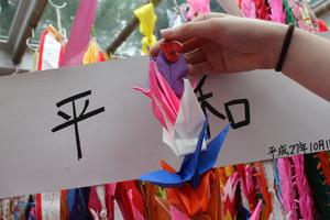 平和と書かれた用紙の前で折り鶴を手に持っている写真