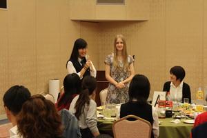 1つの丸テーブルで外国人の女の子と女子高生が2人で立って話をしている写真
