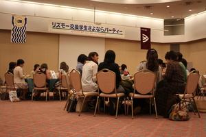 「リズモー交換学生さよならパーティー」と書かれた横断幕、リズモー市と大和高田市の旗が掲げられたホールに集まった参加者達がそれぞれのテーブルに座っている写真