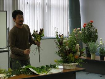 左手に数本の植物を持ちアレンジメントのデモンストレーションを行っているフローリストBee 長岡純一さんの写真