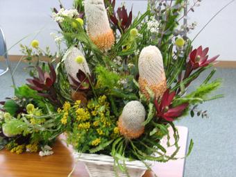 黄色い小さな花や赤い色の花など、複数の植物が使われ完成したフラワーアレンジメントの写真