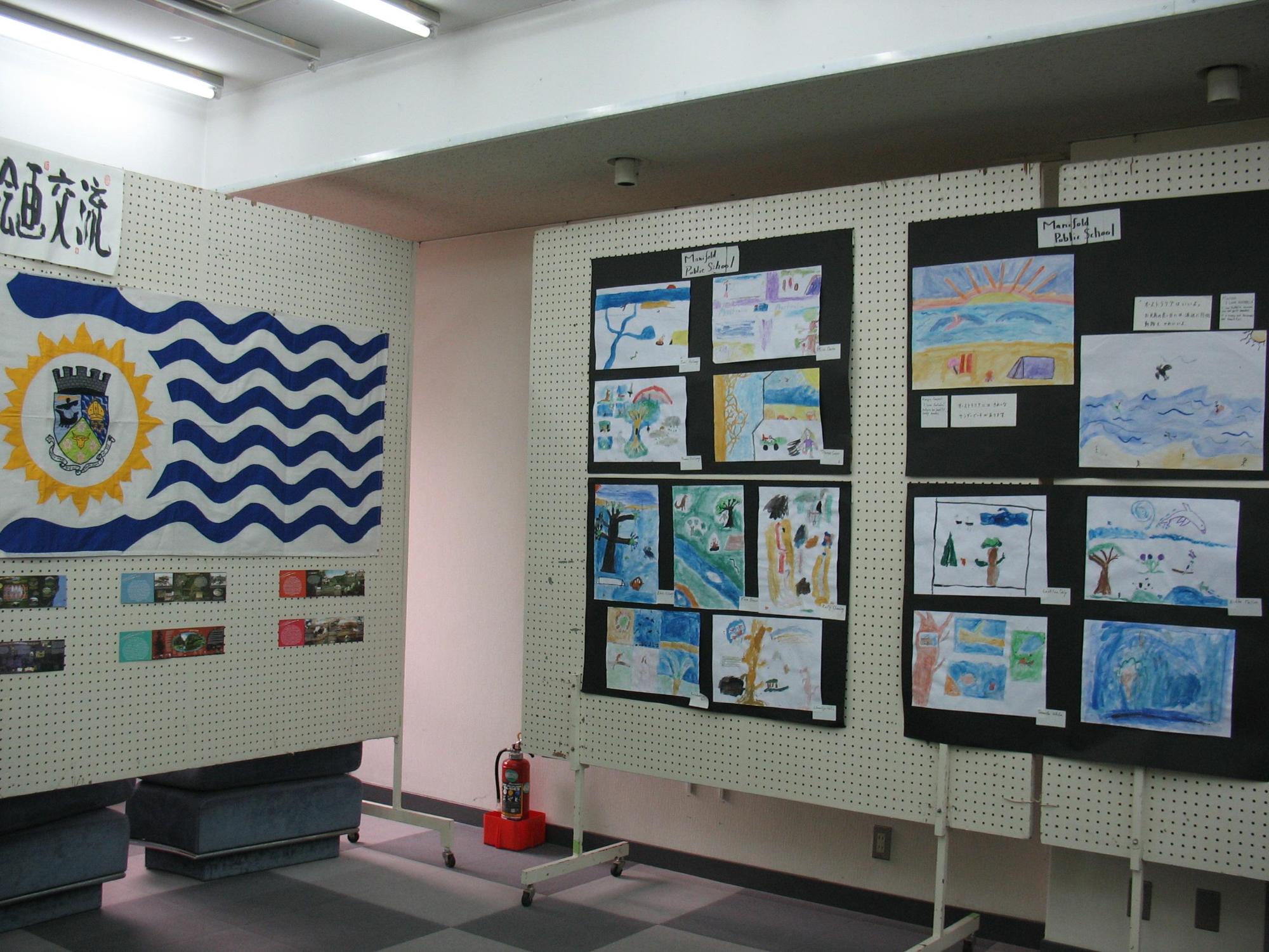 左側に波模様が入った旗が展示されたパネル、右側に海や、木などが描かれた絵が展示されているパネルの写真