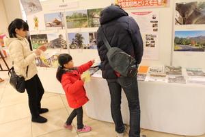 展示の写真を指さししている女の子と、両隣の男性と女性が展示物を見ている写真
