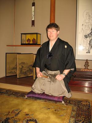 右手に扇子を持ち、座布団に座っている袴姿のキャメロンさんの写真