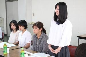一人の女子学生が立っている横に3名の女の人が座っている写真