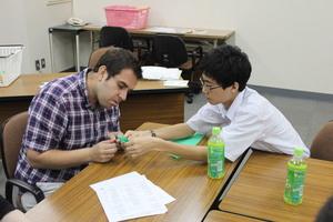1人の男子学生が外国人の男性に折り紙を教えている写真